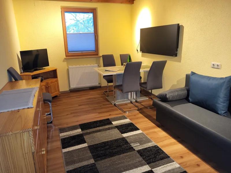 Wohnraum mit Sofa, Essplatz und zwei Fernsehern in Appartement 6