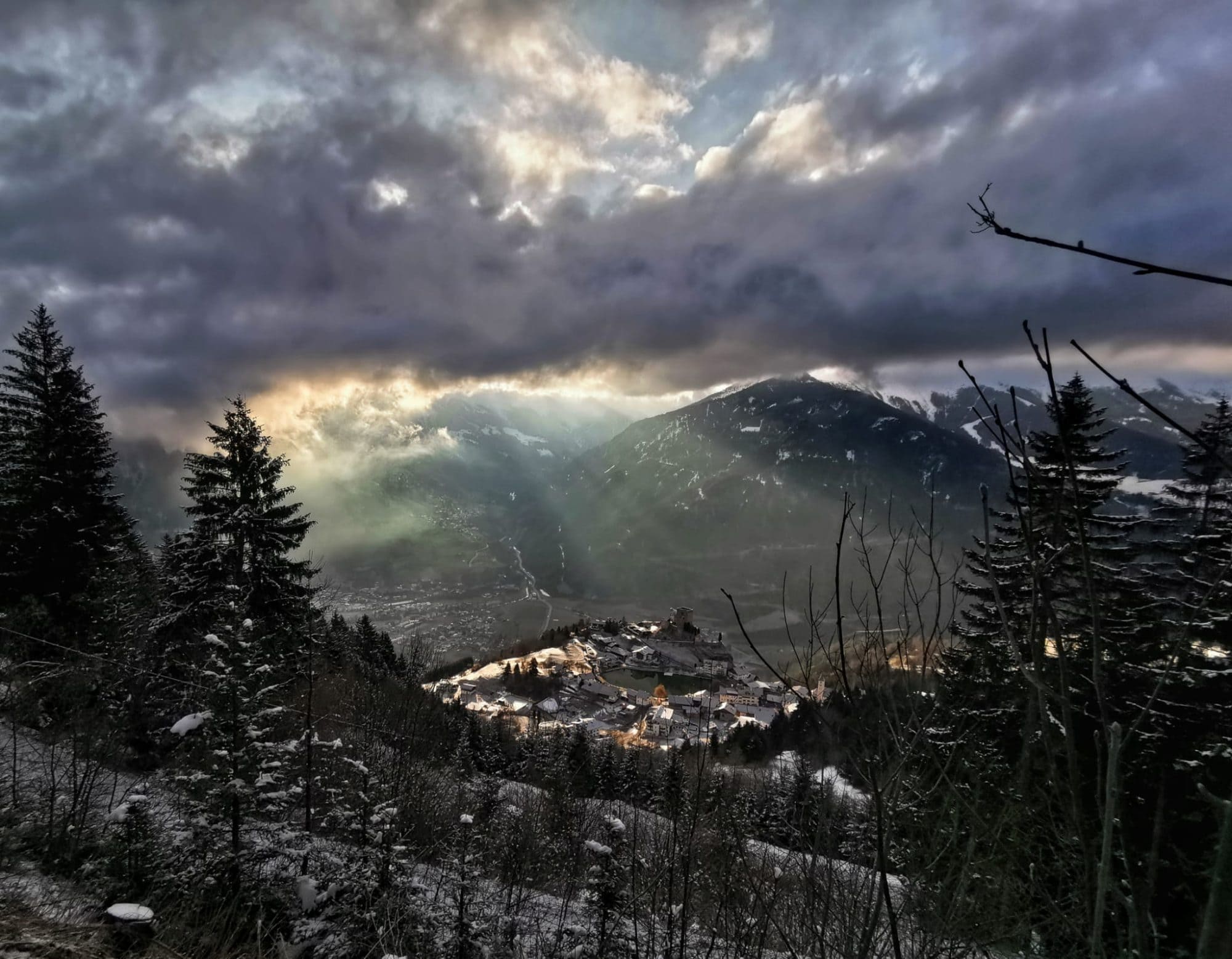 Winterabend über Ladis mit Schloss Laudegg und Sonnenstrahlen durch die Wolken über dem verschneiten Tal