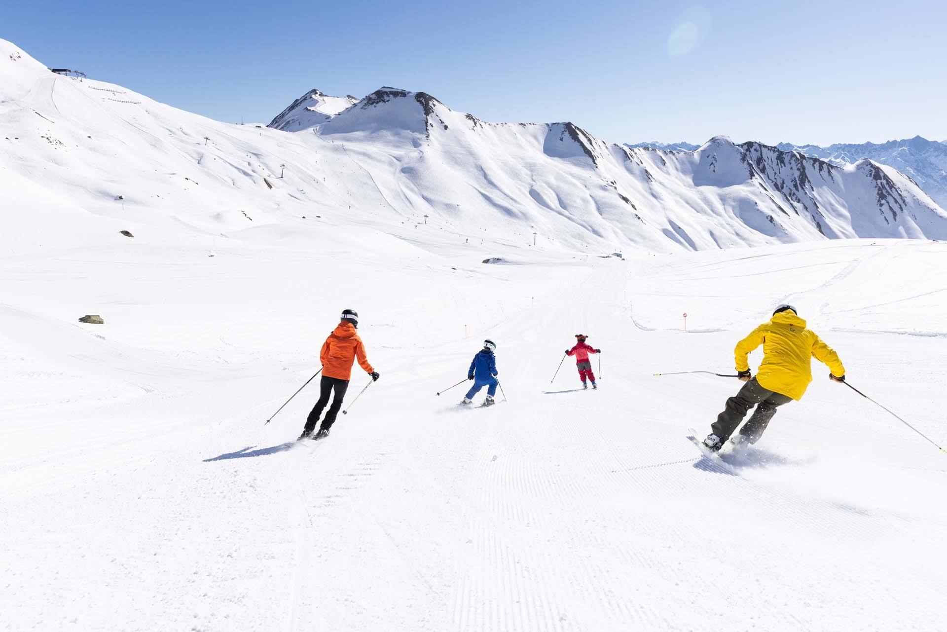 Familie carvt bei blauem Himmel über eine breite, frisch präparierte Piste in Serfaus-Fiss-Ladis