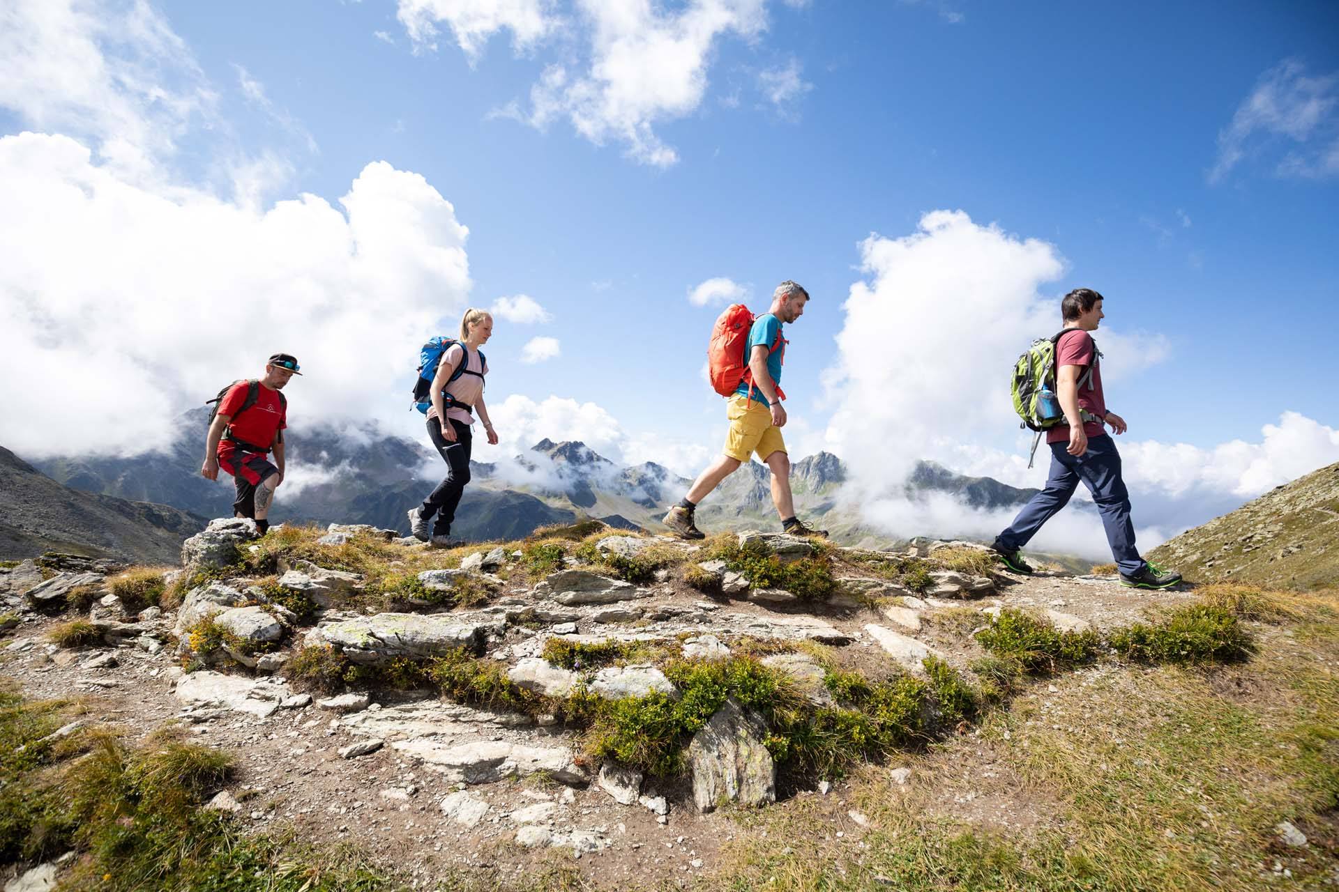 Vier Wanderer gehen auf einem felsigen Gratweg vor Wolken und Bergpanorama in Serfaus-Fiss-Ladis